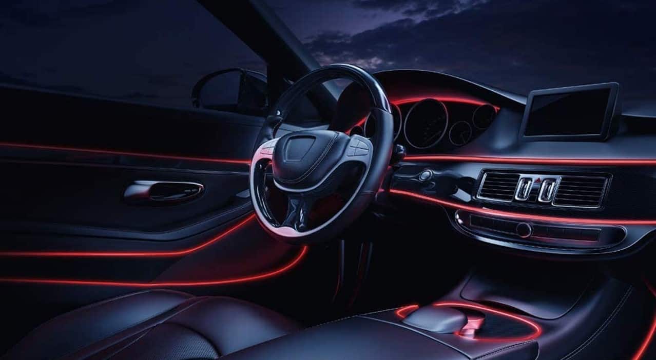 Vehicle interior with red ambient lighting on dashboard and door trim at night